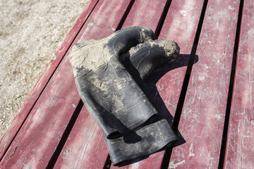 horizontal image of an old pair of black rubber boots full of dried mud lying on a red painted wood step.