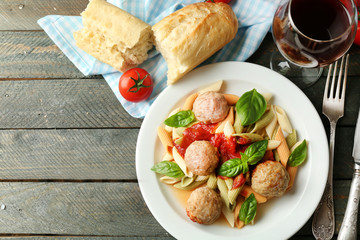 Pasta with meatballs on plate, glass of red wine on wooden  table background