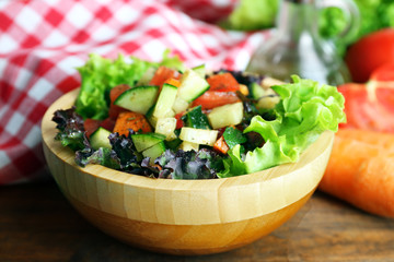 Wooden bowl of fresh vegetable salad on wooden table, closeup