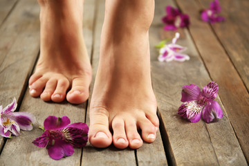 Obraz na płótnie Canvas Female feet with flowers on wooden background