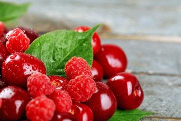 Sweet cherries, raspberries with green leaves on wooden background