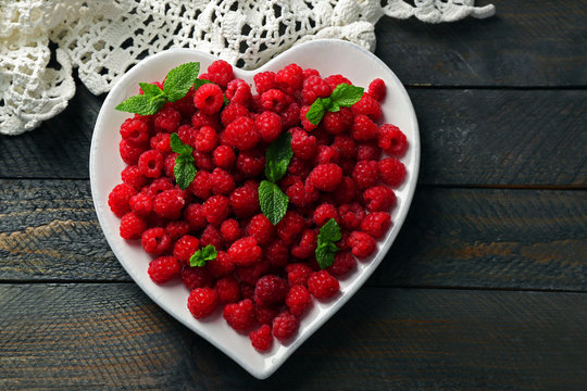 Sweet raspberries on plate, on wooden  background