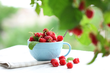 Fresh raspberries in cup on wooden table on blurred nature background