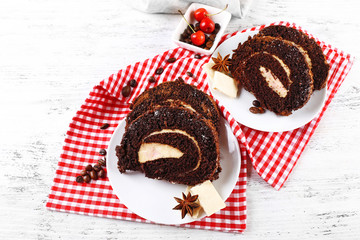Delicious chocolate roll in white saucer on wooden table with checkered napkin, closeup