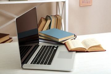 Laptop with books on table in room