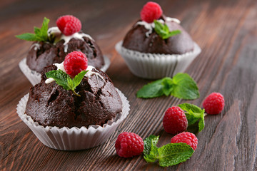 Delicious chocolate cupcakes with berries and fresh mint on wooden table close up