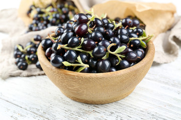 Ripe black currants in wooden bowl on wooden table with sackcloth, closeup