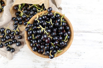 Ripe black currants in wooden bowl on wooden table with sackcloth, top view