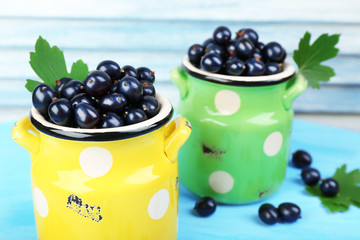 Ripe black currants in metal mugs on wooden background