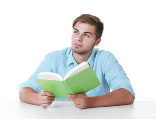 Young man reading book at table on white background