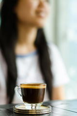 The cup of coffee (espresso) on the wooden table in the coffee shop with woman background