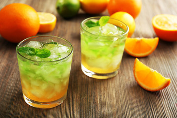Glasses of lime juice with orange on wooden table, closeup