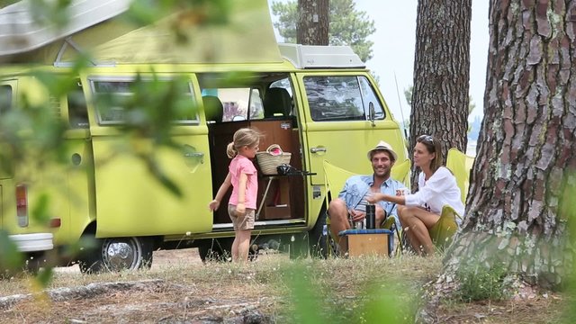 Happy family relaxing by camper van in summer