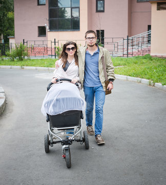 happy man and woman walking with baby pram outdoors