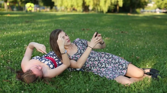 Cute teen girls girlfriends lying on the lawn taking pictures of himself on a mobile phone, selfie.
