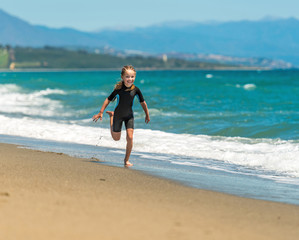 Fototapeta na wymiar girl in a wetsuit running along the beach