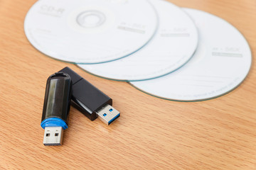 USB flash drives and stacked CDs isolate on wooden background.