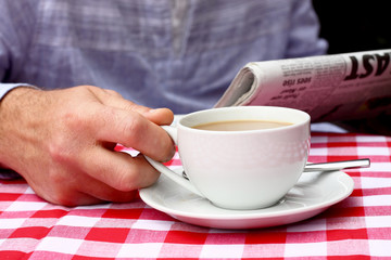Man reading paper cup of tea cafe.
Man reading newspaper outdoors at a café with a cup of tea.
