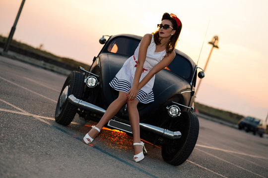 Beautiful pin-up girl with vintage car at sunset road