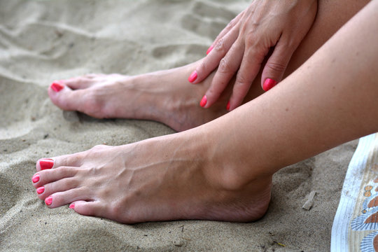 Загорелые женские ножки с красным педикюром на песке
