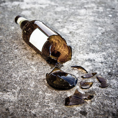Shattered brown beer bottle resting on the ground: alcoholism concept