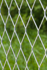 Defocused solid metallic mesh fence against green background