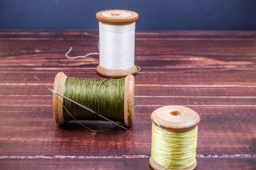 Vintage grunge three wooden thread spool with needle on wooden b