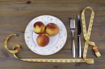 Knife with a fork, plate, tape measure and peaches on a wooden b