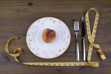 Knife with a fork, plate, tape measure and peach on a wooden bac