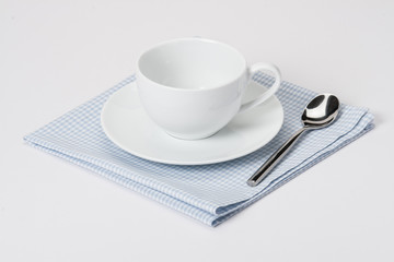 Cup, Plate And Spoon On Folded Gingham Cotton Napkin. White Back