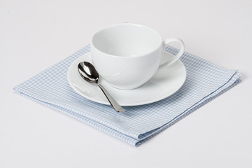 Cup, Plate And Spoon On Folded Gingham Cotton Napkin. White Back