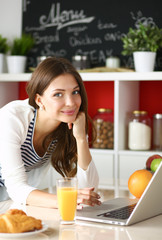 Attractive young woman using laptop and sitting in the kitchen 