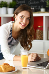 Attractive young woman using laptop and sitting in the kitchen 
