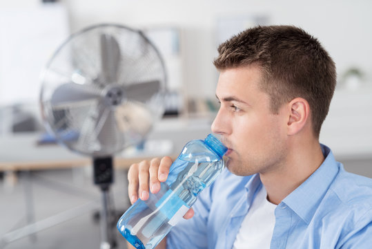 mann trinkt wasser im b&uuml;ro mit ventilator im hintergrund