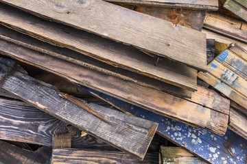 Photograph of old, rotten, scrapped floorboards and decking planks amassed and scattered in a untidy heap.