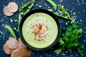 Healthy green soup with ham and peas on a black background