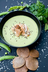 Healthy green soup with ham and peas on a black background