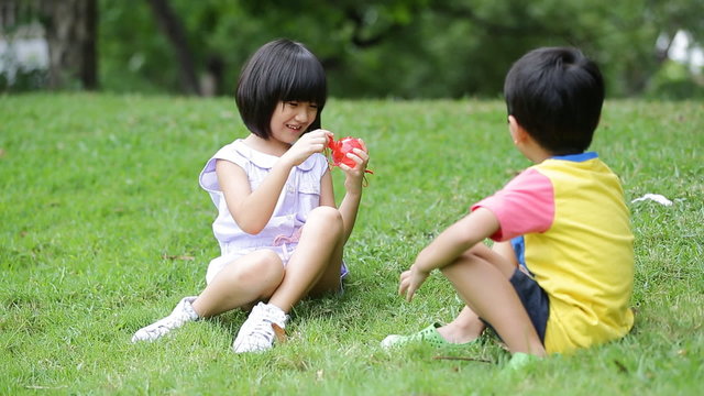 Little asian boy and girl blowing soap bubble in the park