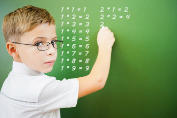 First grade schoolboy wrote multiplication table on blackboard