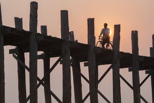 Man on bicycle silhouetted at sunrise crossing Taungthaman Lake on U Bein teak bridge at dawn, Amarapura, Mandalay, Myanmar (Burma), Asia 