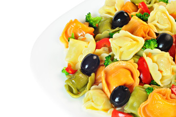 Salad made with tortellini, olives, broccoli, red pepper, on a plate, white background