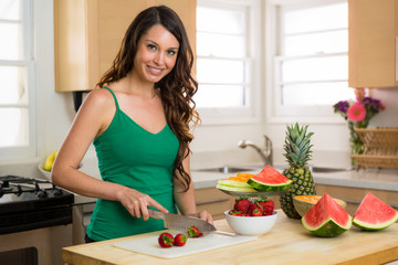 Beautiful woman slicing strawberries in kitchen on cutting board wood bright home smile perfect hair teeth