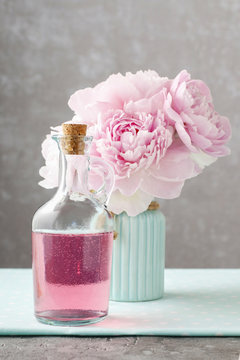 Glass bottle of liquid soap and vase with peonies