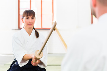 Mann und Frau kämpfen bei Aikido Training in Kampfsportschule mit Holzschwertern
