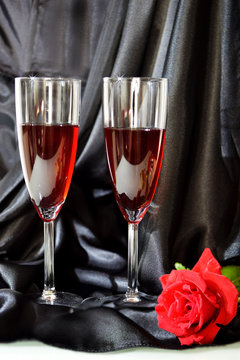 two glasses of red wine, red rose on the background of black silk fabric - romantic greeting card for Valentine's Day