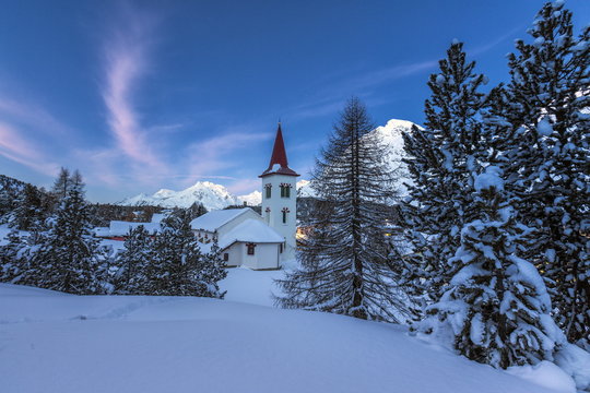 The white church of Maloja Pass in the winter fairy-tale landscape of the Engadine Valley at the blue hour, Graubunden