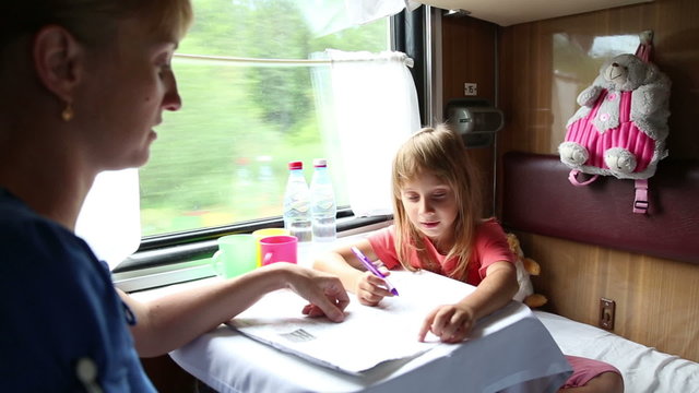 Woman with daughter ride in a train, they sit in the coupe and solve crossword
