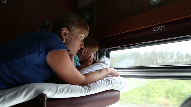Woman with son ride in a train, they lie on the shelf and look out the window
