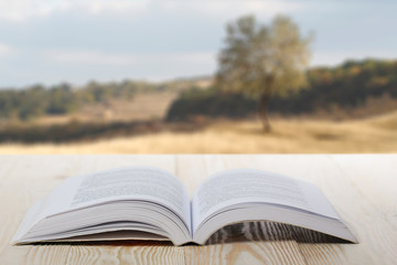 Open book on wooden table on natural blurred background