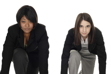 Two serious businesswomen kneeled down as if about to start a race.